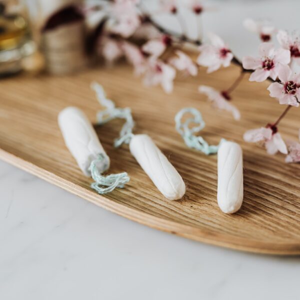 High angle of three menstrual tampons on bamboo plate with flower twig placed against various cosmetic products