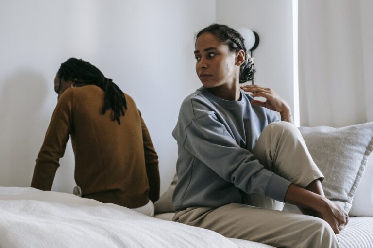 Young African American couple wearing casual outfit sitting on different sides of bed with sad face at home in day