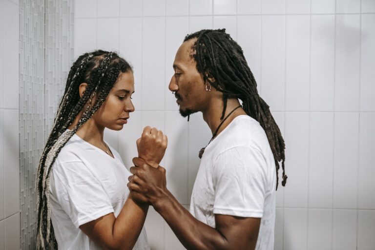 Side view of young muscular African American male holding arm of female partner while struggling in house