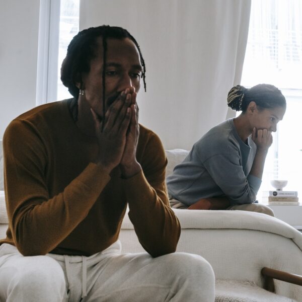 Wistful concerned African American couple in casual clothing sitting on bed at home after having quarrel