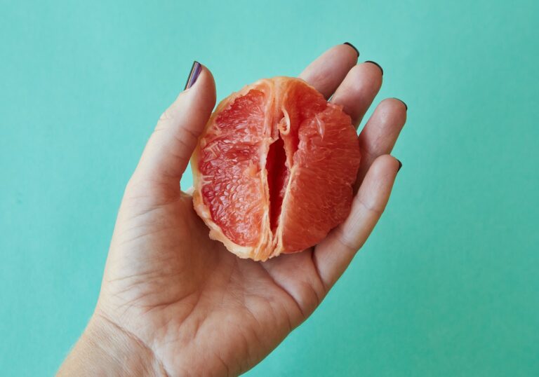 From above of crop anonymous female demonstrating half of juicy peeled grapefruit as vagina against blue background in studio