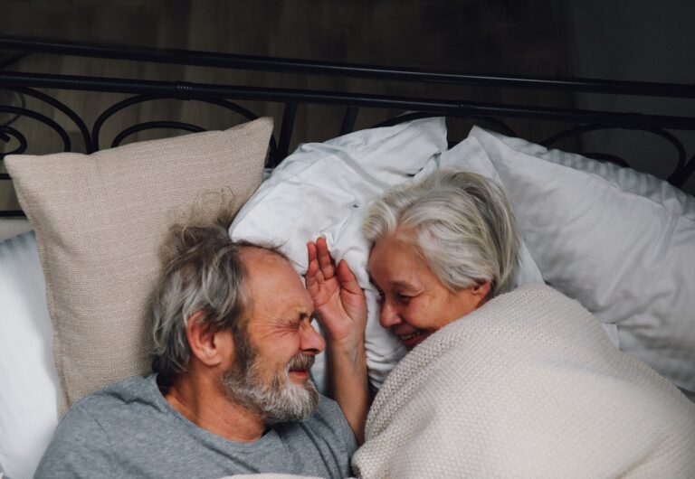 `Elderly Couple Facing Each Other and Smiling in Bed